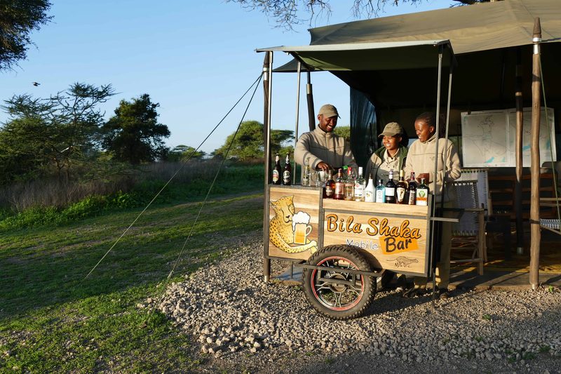 Staff standing behind the Bila Shaka bar cart outside the mess tent