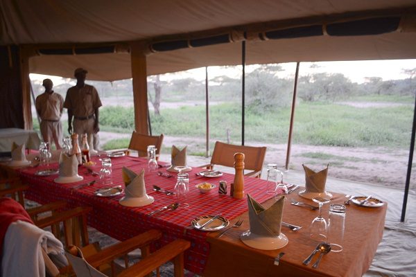 Dining table laid with red cloths inside the mess tent, two staff members at the far end