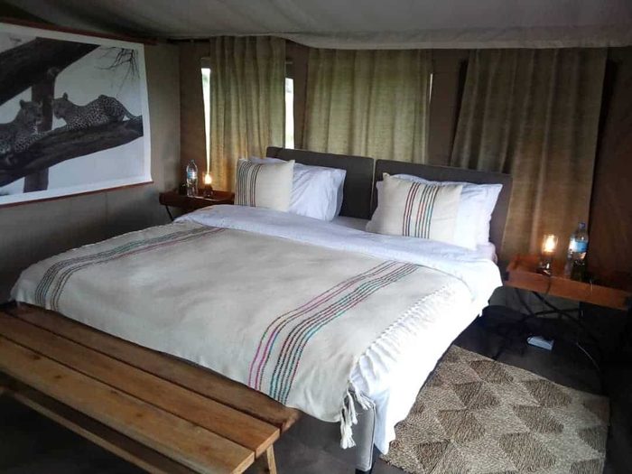 Double bed with a striped throw and a wooden bench in a guest tent, a framed print above