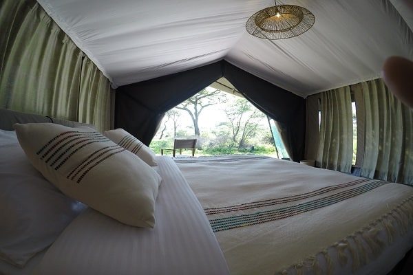 Close view of a made bed with striped cushions in a guest tent, the door open to the trees
