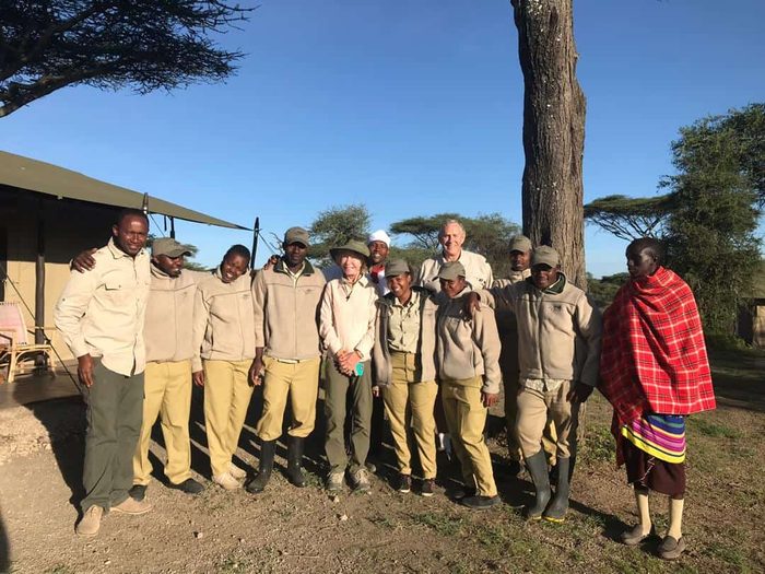 Njozi Camp staff in uniform standing together outside a tent, one man wearing a red Maasai shuka