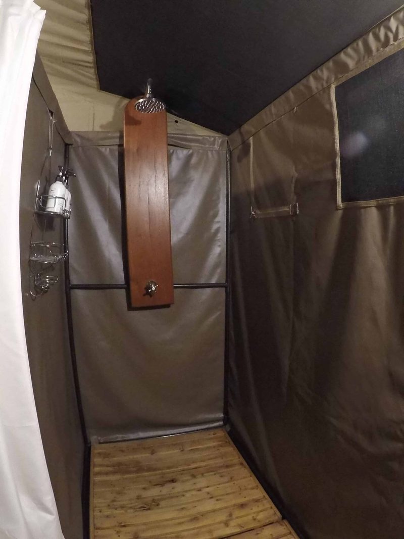 Private shower in a guest tent: canvas walls, a slatted wooden floor and a shower head