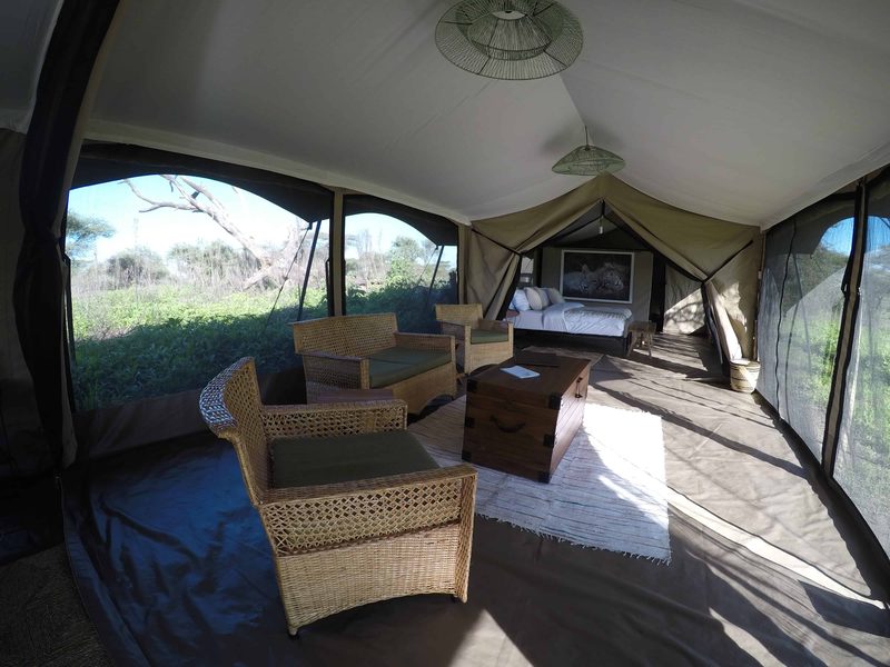 Family tent living room with cane armchairs and a wooden chest, a bedroom beyond