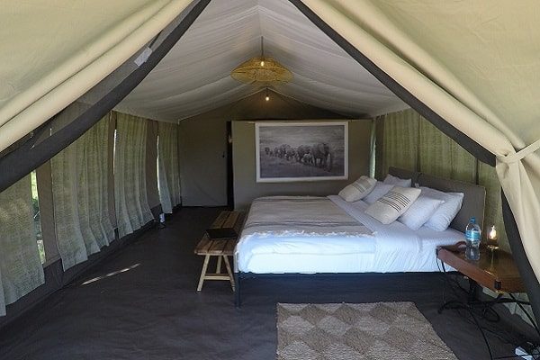 Inside a guest tent: double bed, wooden bench and woven rug under a woven pendant light