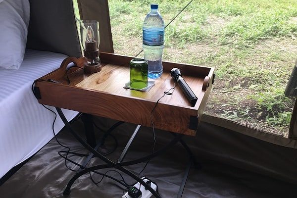 Bedside tray with a water bottle and glass next to a bed in a guest tent