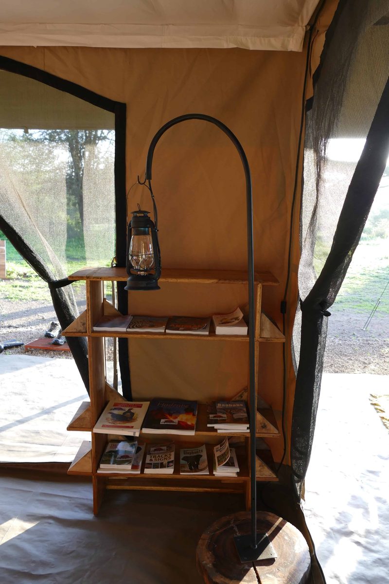 A lantern on a hook beside a shelf of books in the lounge tent