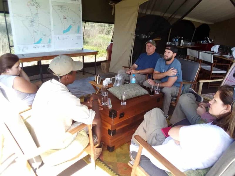Guests relaxing in the lounge tent around a wooden chest, a map of the region on the wall behind